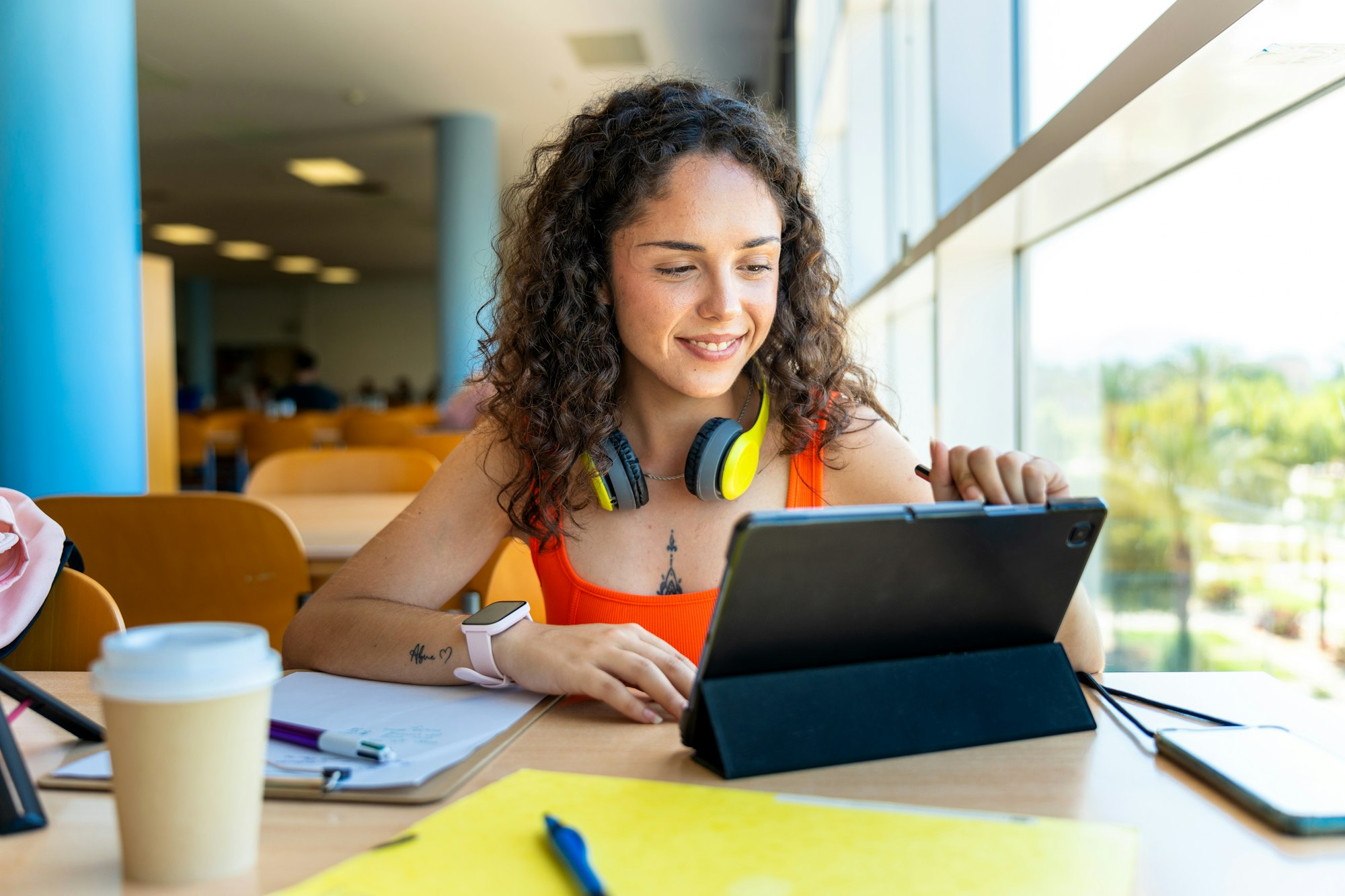 Young curly haired girl smiling using tablet in university library